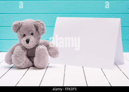 Teddy bear sitting on white wooden floor in blue-green background with blank note Stock Photo