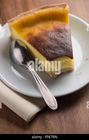 One slice of French 'Flan pâtissier' or 'Parisian Flan' (French custard pie) on a white plate with spoon, one bite taken out. Stock Photo