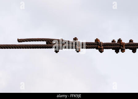 Pair of rusted metal cables held together with several brackets and screws on white sky. Stock Photo