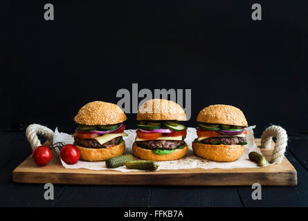 Fresh homemade burgers on wooden serving board over black  background. Stock Photo