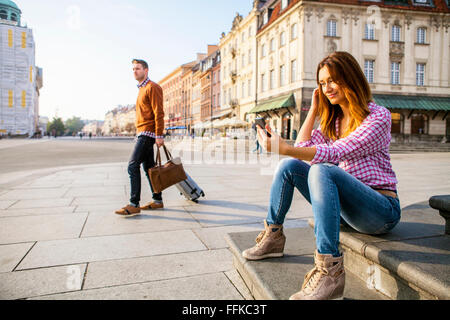 Mid adult woman using smart phone with man in background Stock Photo