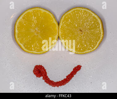 Lemon cut in half on a plate with sugar, arranged to look like a smiley face with a mouth made from tomato puree Stock Photo