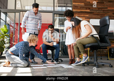Creative people looking at project plan laid out on floor. Mixed race business associates discussing new project plan in modern Stock Photo