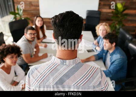Rear view portrait of man giving business presentation to colleagues in conference room.  Young people meeting in boardroom. Stock Photo