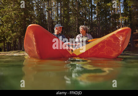 Active senior couple in two single kayaks side by side. Mature man and woman looking at each other and smiling while kayaking in Stock Photo