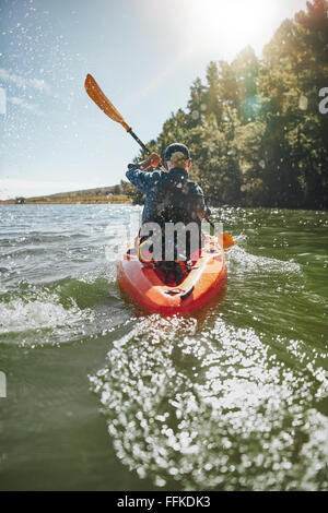 Rear view image of a mature man canoeing in a lake on a sunny day. Senior man paddling a kayak. Stock Photo