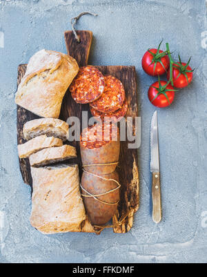 Wine snack set. Hungarian mangalica pork salami sausage, rustic bread and fresh tomatoes on dark wooden board over a rough grey- Stock Photo