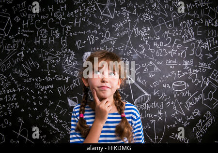 Girl  thinking, finger on cheek, blackboard with mathematical sy Stock Photo