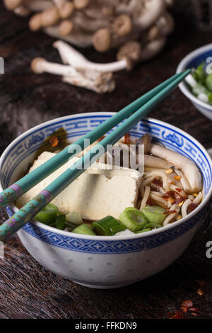 Chinese porcelain bowl of asian ramen soup with feta cheese, noodles, spring onion and mushrooms, served with turquoise chopstic Stock Photo