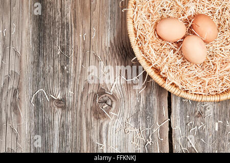 Top view of easter nest with three raw uncolored brown eggs on a wooden table. Stock Photo