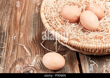 Three fresh eggs in an easter basket and one egg on the wooden table. Stock Photo