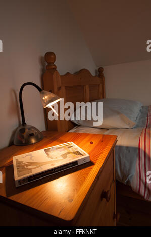 neat wooden pine bed and duvet with cabinet and lamp ready for a good bedside read of a novel Stock Photo