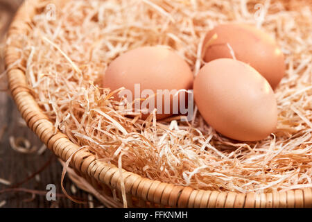 Macro of three raw eggs in an easter nest with straw in a basket. Stock Photo
