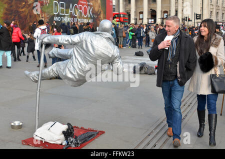 London, UK, 15 February 2016, a couple pass a human statue appearing to float unsupported  in Trafalgar Square. Stock Photo