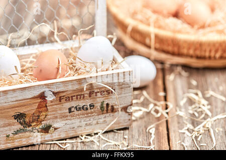 Eggs in an wooden egg box on a wooden talbe with nest in background Stock Photo