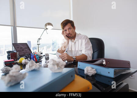 Corporate manager in modern office tries to write a job letter. The man is frustrated and keeps on screwing paper on desk Stock Photo