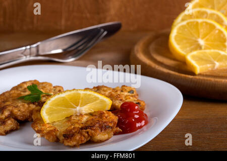 Ketchup with a wiener schnitzel and lemon slices on white plate with wooden background Stock Photo