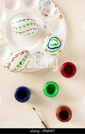 Natural white eggs with various patterns painted by hand for Easter with art supplies. Festive background with natural light. Stock Photo