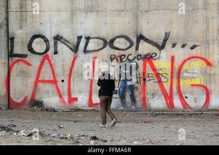 Calais, France. 10th Feb, 2016. A man passes by the graffiti 'LONDON CALLING' phoning on his smartphone. The iconic Banksy graffiti near the Calais migrant camp known as 'The Jungle' has  been vandalised with the words 'London Calling'. The words 'London Calling'  in giant lettering over the top of the image - using the figure of Steve Jobs as the 'I'. Stock Photo