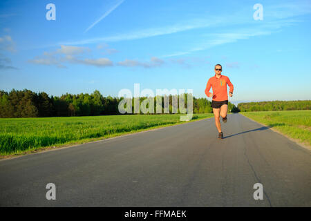 Man runner running on country road, training inspiration and motivation in summer sunset. Young athlete male training and doing Stock Photo