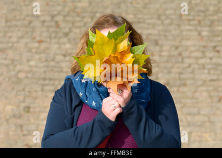 Woman posing with bunch of maple tree leaves with autumnal colours in front of face Stock Photo