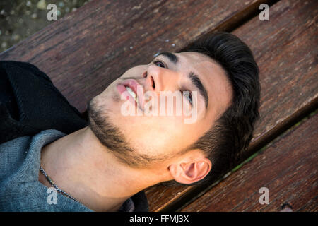 Close-up of young man relaxing on bench and looking up, smiling Stock Photo