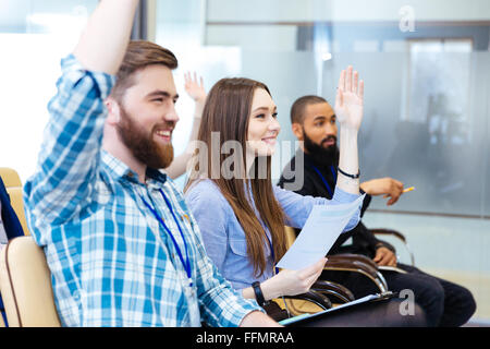 Cheerful young people sitting with raised hands and asking questions on business conference Stock Photo