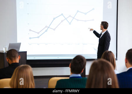 Confident speaker giving public presentation using projector in conference room Stock Photo