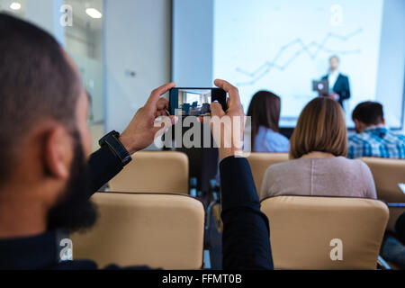 Back view of young african man making video with smartphone on business conference in meeting room Stock Photo