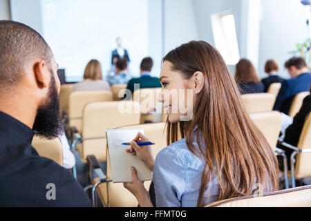 Back view of two young smiling people writing and talking on business meeting in conference hall Stock Photo