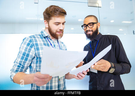 Two happy modern business men talking and looking at documents in office Stock Photo