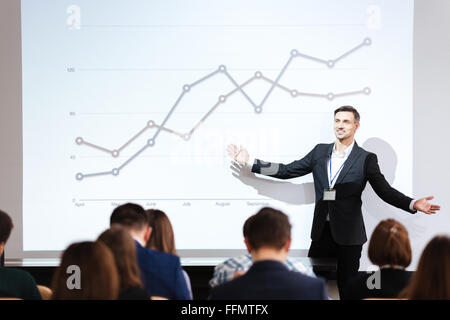 Smiling charismatic speaker giving public presentation in conference hall Stock Photo