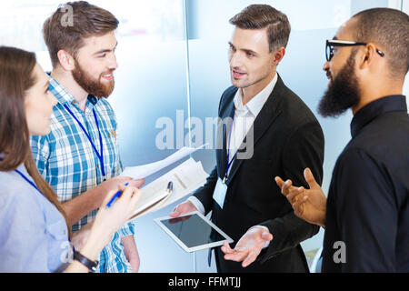 Multiethnic group of young business people standing and talking with chief executive in office Stock Photo