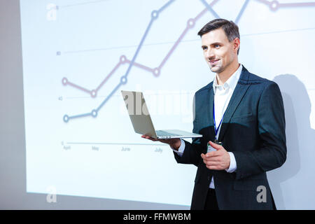 Happy speaker holding laptop and giving presentation in conference hall Stock Photo