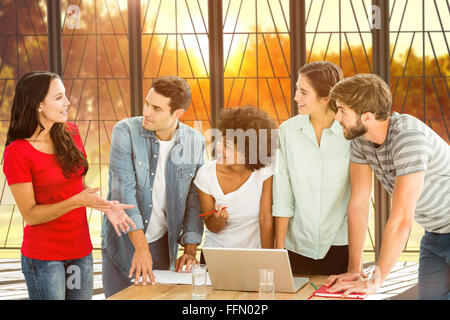 Composite image of colleagues gathered around a laptop at office Stock Photo