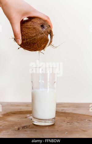 Pouring milk from a coconut into a glass on a wooden table Stock Photo
