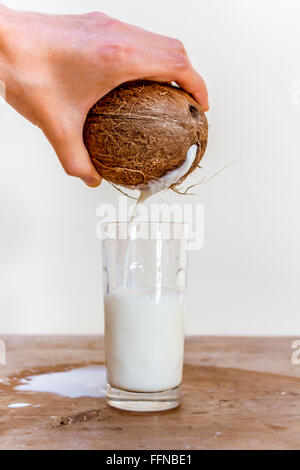 Pouring milk from a coconut into a glass on a wooden table Stock Photo