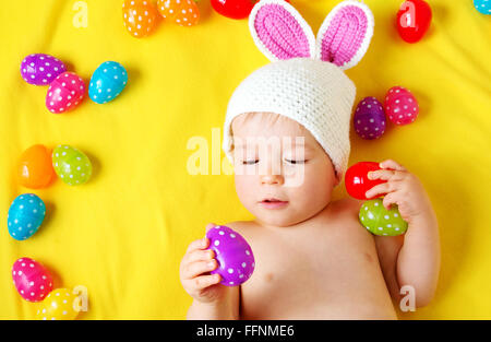 Baby boy in bunny hat lying on yellow blanket with easter eggs Stock Photo