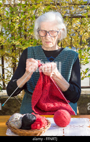 90 years old woman knitting a red sweater outdoors Stock Photo