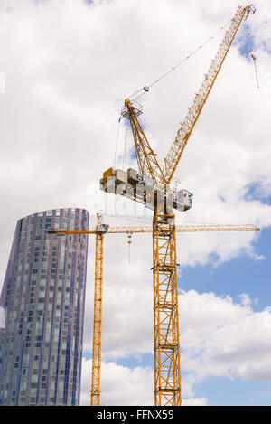 Two big construction cranes with skyscraper and cloudy sky in the background Stock Photo