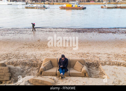 Sculptor sitting on a sand sofa sculpture on the Embankment of the River Thames, London at low tide Stock Photo