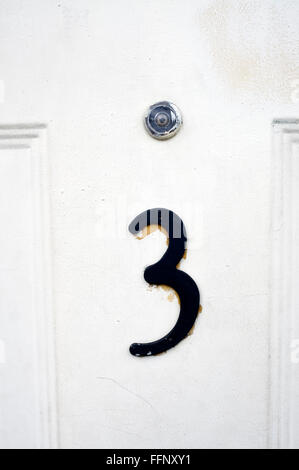 House number three on a white wooden door with a peephole Stock Photo