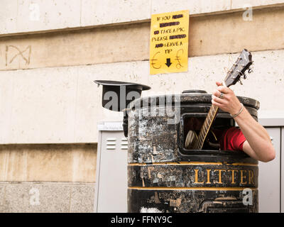 Busker singing and playing guitar inside a rubbish bin on a street. Stock Photo