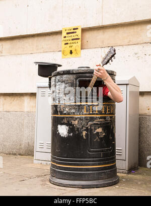 Busker singing and playing guitar inside a rubbish bin on a street. Stock Photo