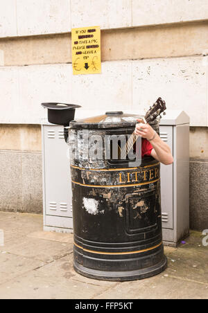 Busker singing and playing guitar inside a rubbish bin on a street. Stock Photo