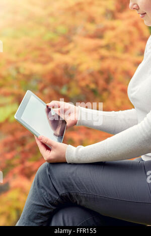 Woman holding a tablet PC in the autumn park. Vertically composed and cross-processed image with color toning Stock Photo