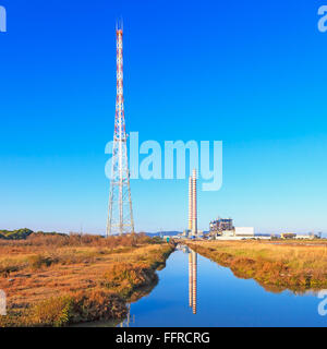 Power plant with two smoke stacks,  transmission tower, green field and reflection on water Stock Photo