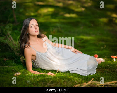 Beautiful woman dressed as a fairy sits on green moss with the poisonous Amanita looking Stock Photo