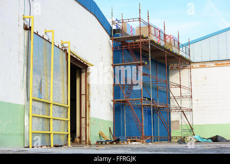 Kallinge, Sweden - February 07, 2016: Scaffoldings stand against an industrial building with packets of insulation on top. Build Stock Photo