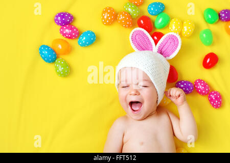 Baby boy in bunny hat lying on yellow blanket with easter eggs Stock Photo